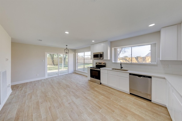 kitchen featuring white cabinets, appliances with stainless steel finishes, decorative backsplash, sink, and hanging light fixtures