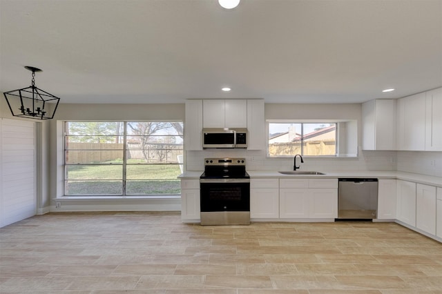 kitchen featuring appliances with stainless steel finishes, white cabinets, decorative light fixtures, and sink