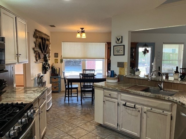 kitchen with sink, an inviting chandelier, stainless steel appliances, light tile patterned floors, and light stone counters