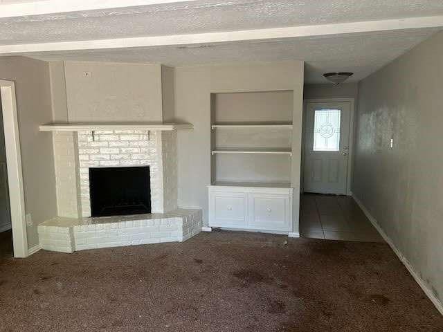 unfurnished living room with a brick fireplace, a textured ceiling, built in features, and carpet flooring