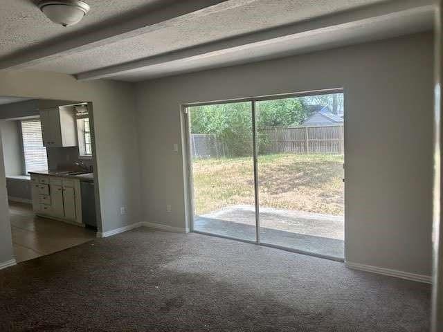 unfurnished living room with sink, a textured ceiling, beamed ceiling, and carpet flooring