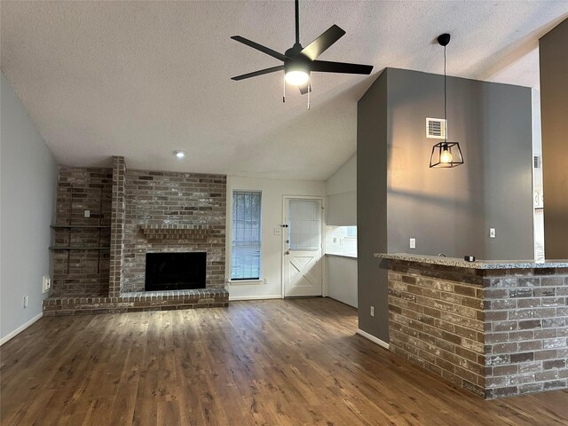 unfurnished living room featuring ceiling fan, vaulted ceiling, a fireplace, dark wood-type flooring, and a textured ceiling