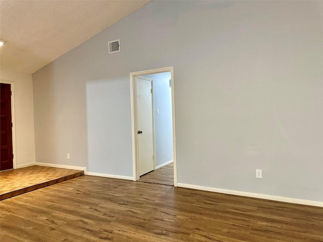 spare room featuring lofted ceiling, dark hardwood / wood-style flooring, and a textured ceiling