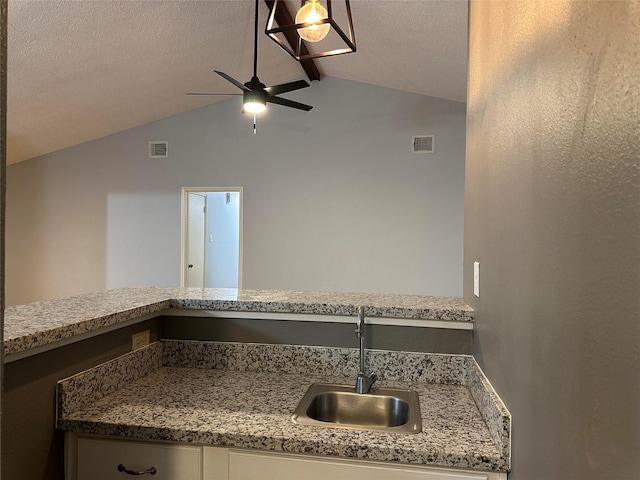 kitchen featuring ceiling fan, lofted ceiling with beams, sink, a textured ceiling, and stone countertops