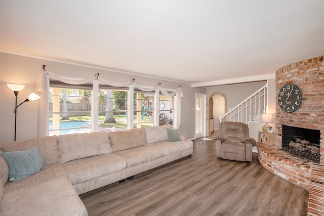 living room featuring wood-type flooring, a brick fireplace, and ornamental molding