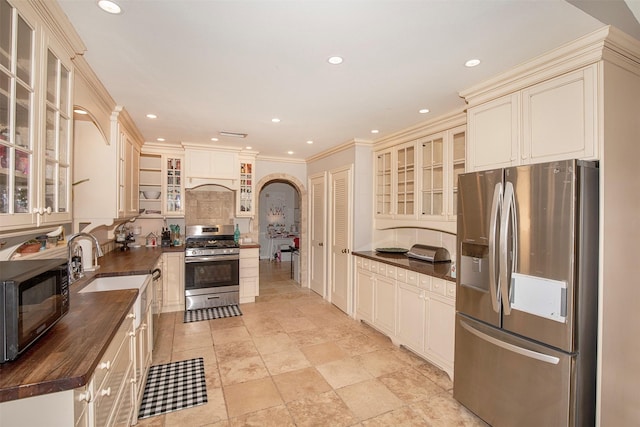 kitchen with wooden counters, stainless steel appliances, crown molding, and cream cabinets