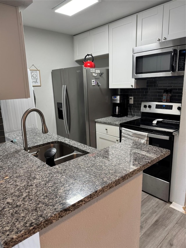 kitchen with light hardwood / wood-style floors, stainless steel appliances, dark stone countertops, white cabinets, and sink