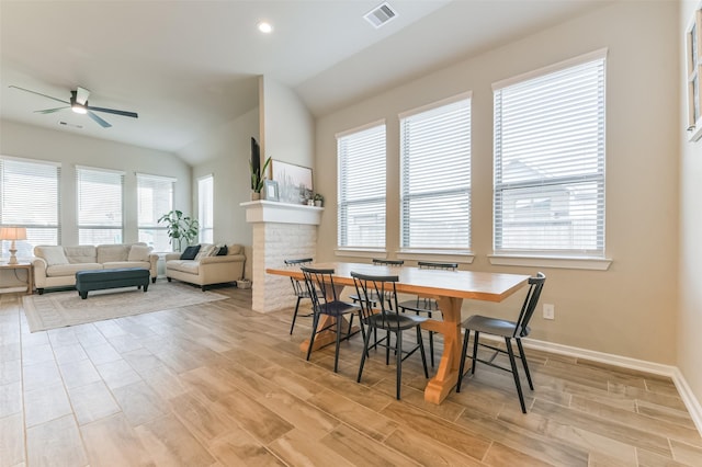 dining space with ceiling fan, lofted ceiling, and a brick fireplace