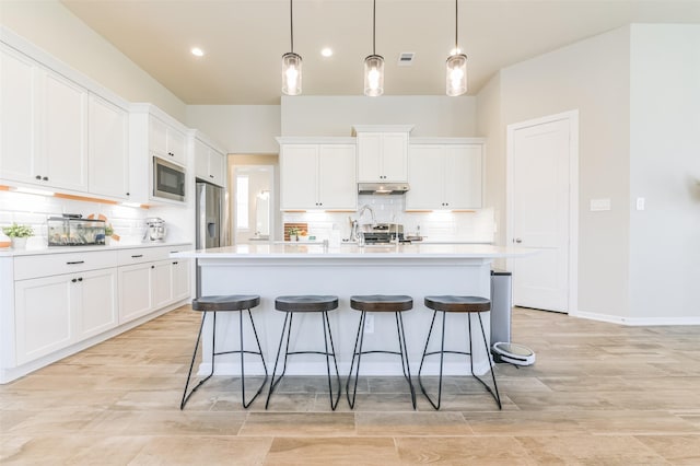 kitchen featuring an island with sink, hanging light fixtures, white cabinets, and built in microwave