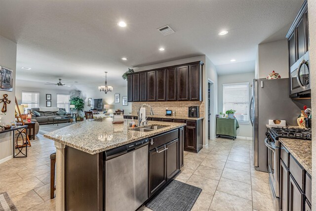 kitchen with a center island with sink, sink, appliances with stainless steel finishes, dark brown cabinets, and ceiling fan with notable chandelier