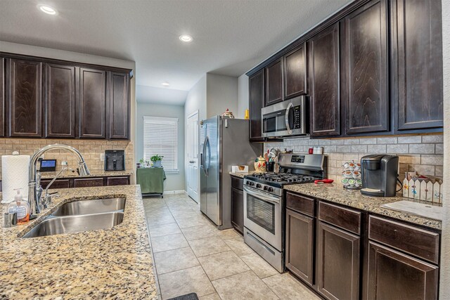 kitchen featuring light stone counters, sink, stainless steel appliances, and dark brown cabinets