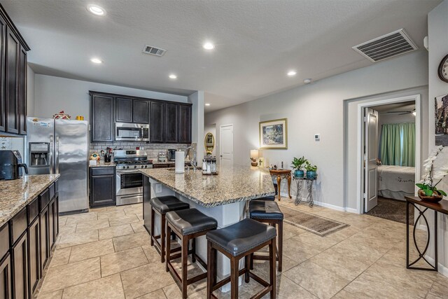 kitchen with an island with sink, appliances with stainless steel finishes, tasteful backsplash, light stone countertops, and a breakfast bar