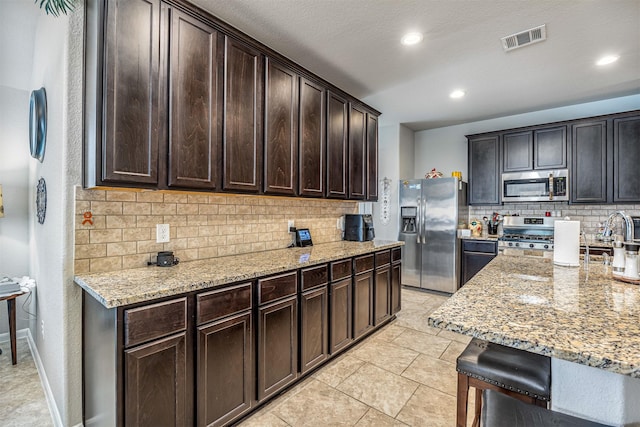 kitchen featuring light tile patterned floors, stainless steel appliances, dark brown cabinets, and light stone counters