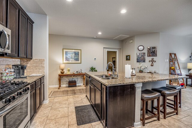 kitchen with dark brown cabinets, light stone countertops, an island with sink, and sink