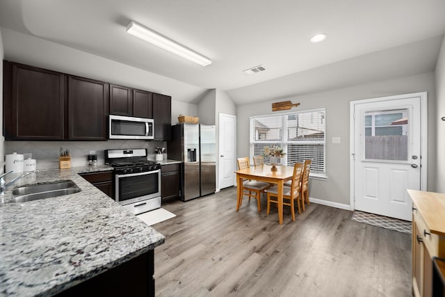 kitchen featuring light stone countertops, dark brown cabinetry, appliances with stainless steel finishes, sink, and vaulted ceiling