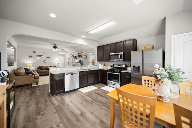 kitchen with kitchen peninsula, ceiling fan, appliances with stainless steel finishes, dark brown cabinets, and light stone counters