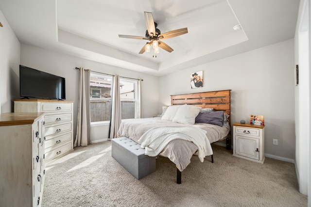 bedroom with ceiling fan, light colored carpet, and a tray ceiling