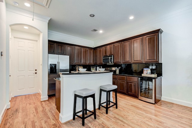 kitchen with dark brown cabinetry, appliances with stainless steel finishes, a kitchen island, wine cooler, and tasteful backsplash