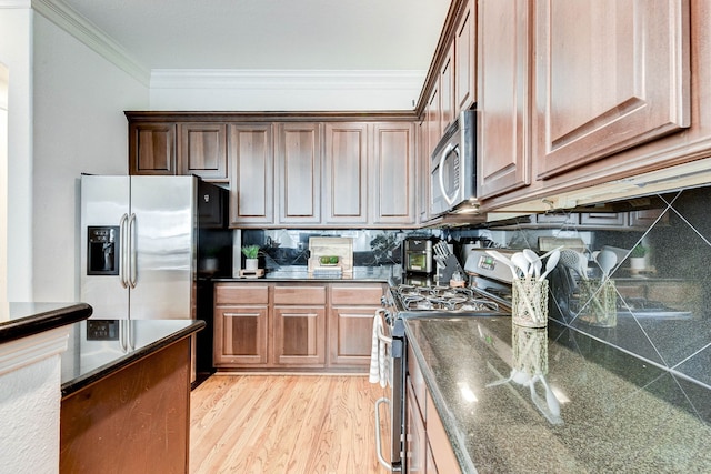 kitchen featuring appliances with stainless steel finishes, dark stone counters, backsplash, light wood-type flooring, and crown molding