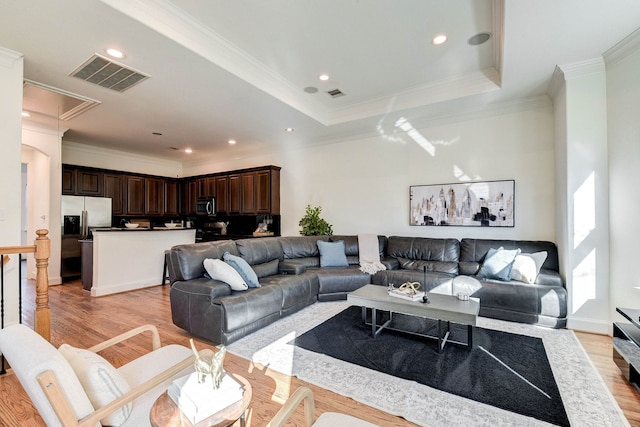 living room featuring a raised ceiling, ornamental molding, and light hardwood / wood-style flooring