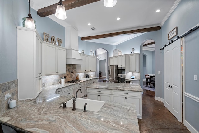 kitchen featuring arched walkways, a barn door, stainless steel appliances, a sink, and light stone countertops