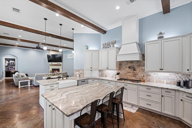 kitchen featuring custom range hood, stainless steel gas stovetop, a sink, a warm lit fireplace, and a peninsula