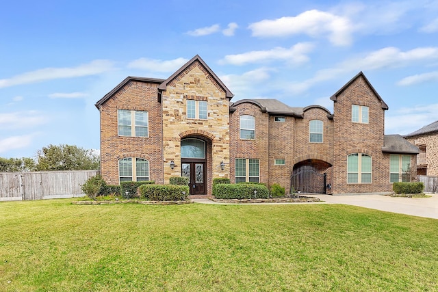 traditional-style house featuring brick siding, concrete driveway, a front yard, fence, and stone siding