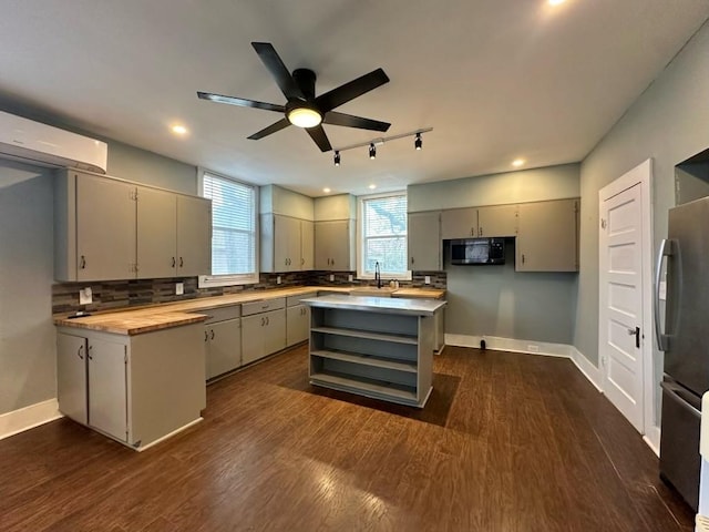 kitchen featuring butcher block countertops, dark wood-type flooring, stainless steel fridge, a kitchen island, and decorative backsplash