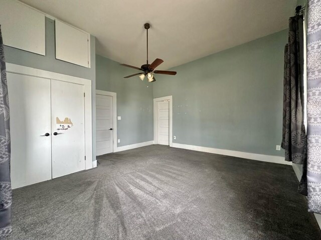 unfurnished bedroom featuring dark colored carpet, a towering ceiling, and ceiling fan