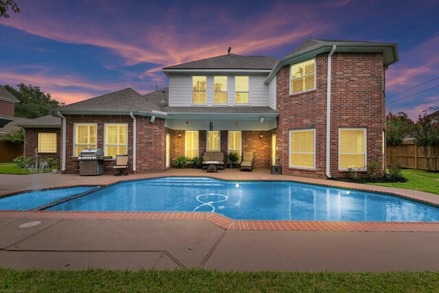 pool at dusk featuring a grill and a patio area