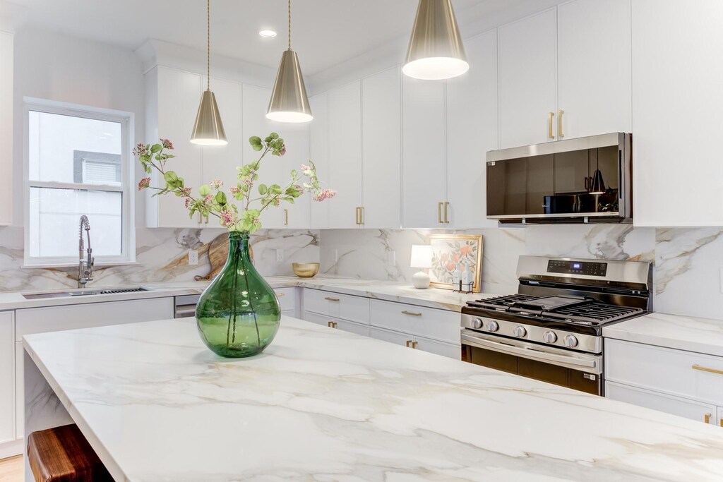 kitchen with light stone counters, sink, decorative light fixtures, and gas stove