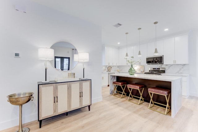 kitchen featuring decorative light fixtures, tasteful backsplash, white cabinetry, a breakfast bar area, and stainless steel range oven