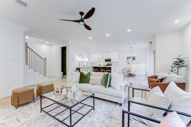 living room featuring ceiling fan with notable chandelier and light wood-type flooring