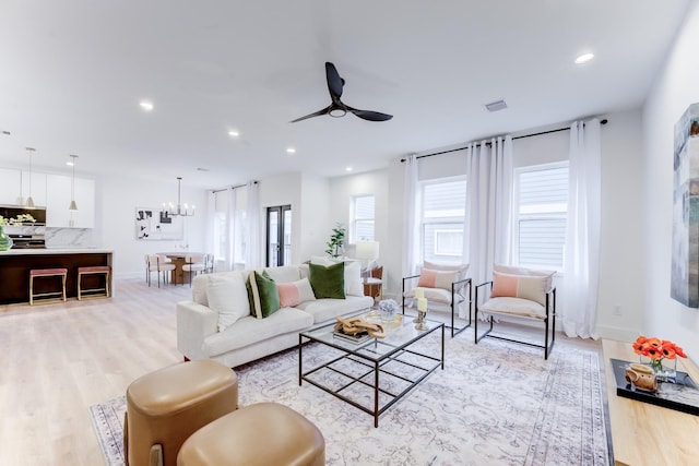 living room with ceiling fan with notable chandelier and light wood-type flooring