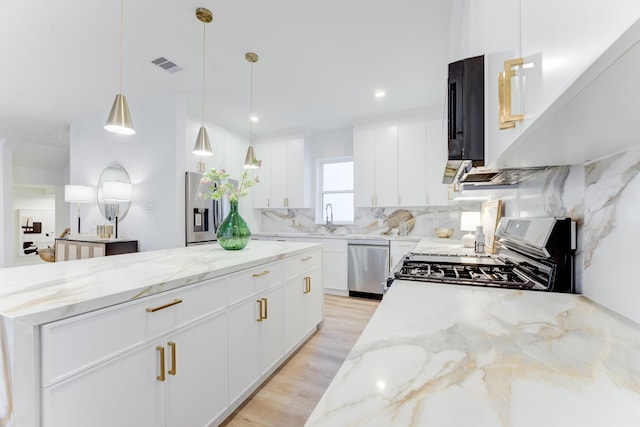 kitchen featuring light stone counters, stainless steel appliances, hanging light fixtures, and white cabinets