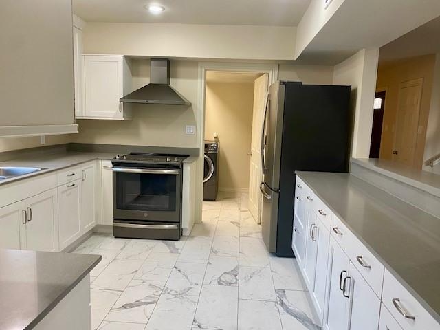 kitchen with white cabinets, washer / clothes dryer, wall chimney exhaust hood, and appliances with stainless steel finishes