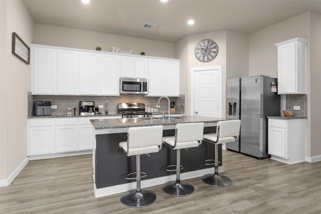 kitchen featuring white cabinets, stainless steel appliances, an island with sink, sink, and light wood-type flooring