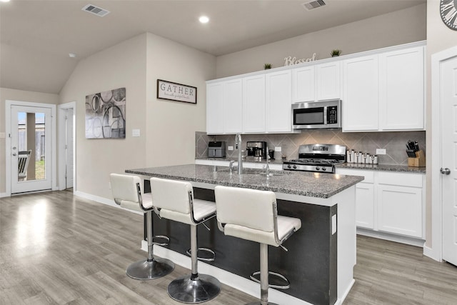 kitchen with white cabinets, appliances with stainless steel finishes, dark stone counters, and a center island with sink