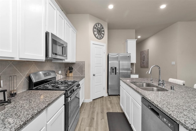 kitchen with white cabinetry, stainless steel appliances, light stone counters, and sink