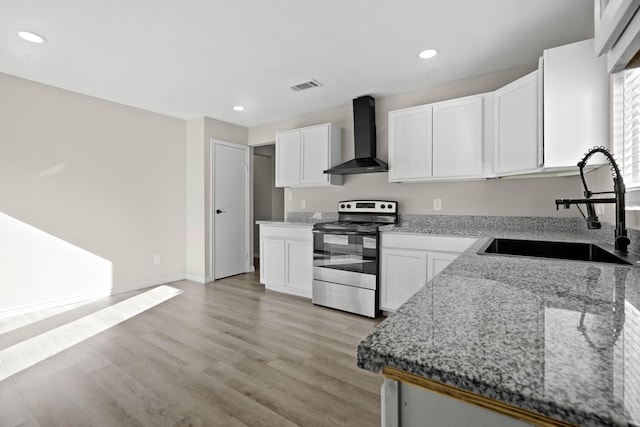 kitchen featuring stainless steel range with electric cooktop, wall chimney range hood, light stone countertops, white cabinets, and sink