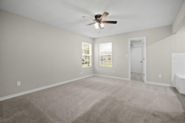 unfurnished bedroom with ceiling fan, a walk in closet, a closet, and light colored carpet