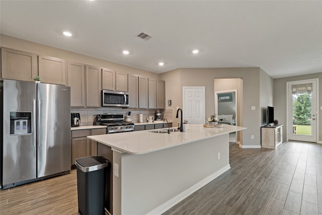 kitchen featuring a center island with sink, gray cabinets, stainless steel appliances, decorative backsplash, and sink