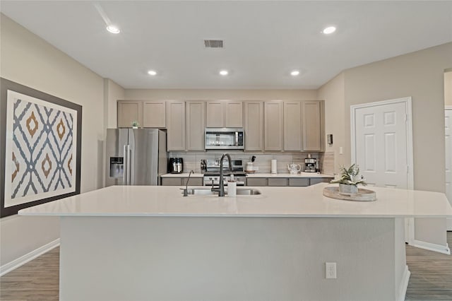 kitchen featuring hardwood / wood-style floors, appliances with stainless steel finishes, decorative backsplash, a spacious island, and sink