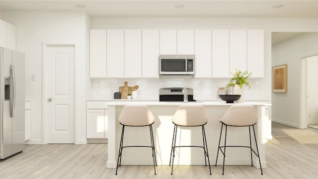 kitchen featuring white cabinets, appliances with stainless steel finishes, a breakfast bar area, and a center island with sink