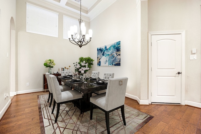 dining space featuring an inviting chandelier, a towering ceiling, crown molding, and hardwood / wood-style floors