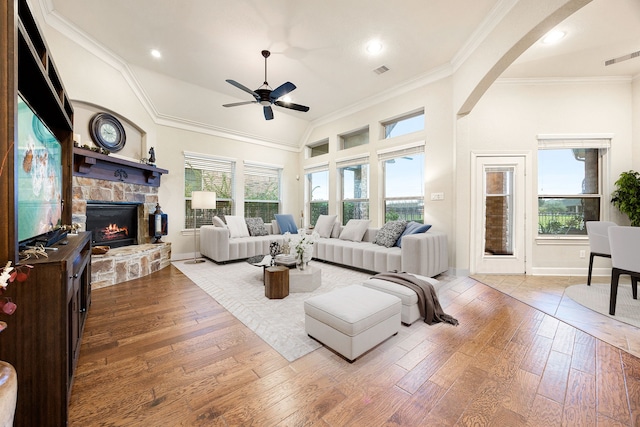 living room featuring ceiling fan, vaulted ceiling, a stone fireplace, and hardwood / wood-style flooring