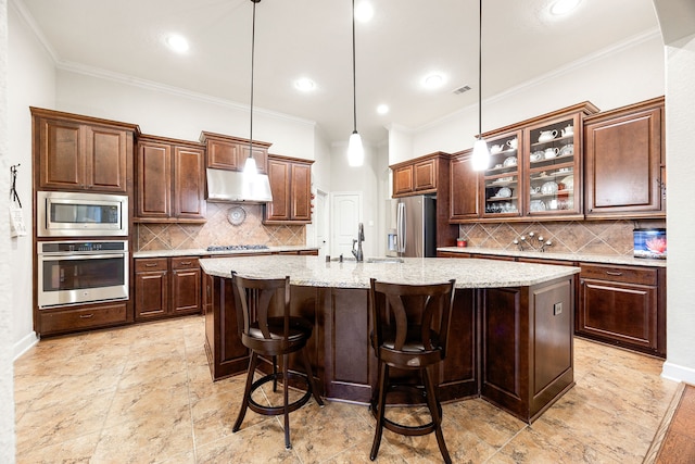 kitchen with hanging light fixtures, appliances with stainless steel finishes, a center island with sink, and tasteful backsplash