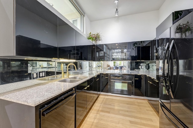 kitchen with a high ceiling, light stone countertops, black appliances, and light hardwood / wood-style flooring