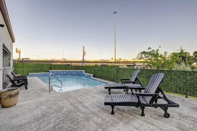 pool at dusk with pool water feature and a patio area