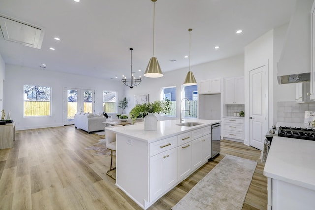 kitchen with an island with sink, tasteful backsplash, wall chimney exhaust hood, white cabinets, and sink